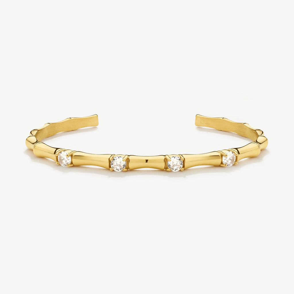 Gold cuff bracelet with bamboo-inspired design and four round clear gemstones on white background