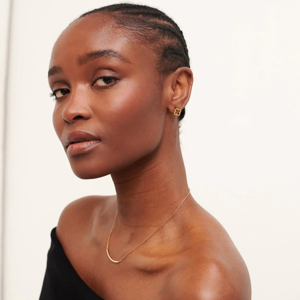 Close-up portrait of a woman wearing gold clover earrings and a delicate gold necklace in a minimalist setting