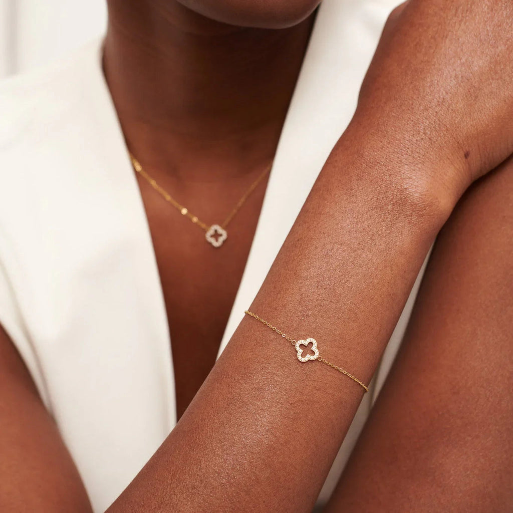 Close-up of woman wearing gold clover pendant necklace and matching bracelet with white top