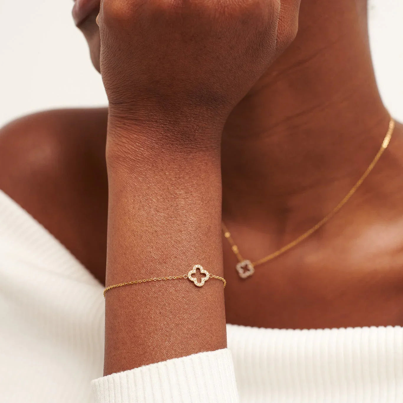 Close-up of woman wearing gold bracelet and necklace with clover-shaped diamond pendants