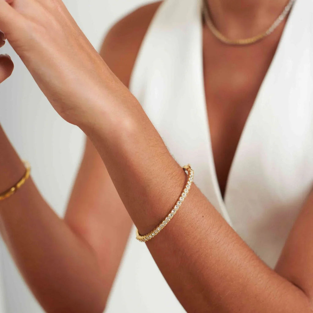 Close-up of a woman wearing a gold and diamond tennis bracelet and a white sleeveless top