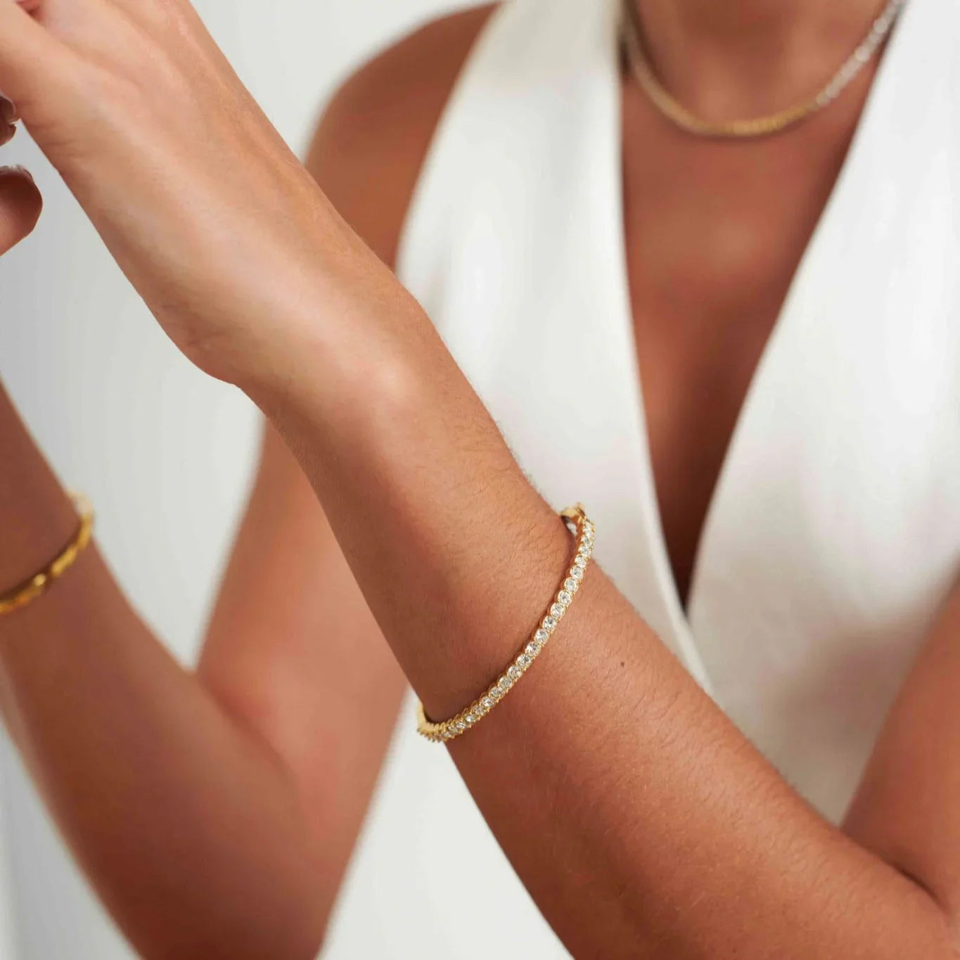 Close-up of a woman wearing a gold and diamond tennis bracelet and a white sleeveless top