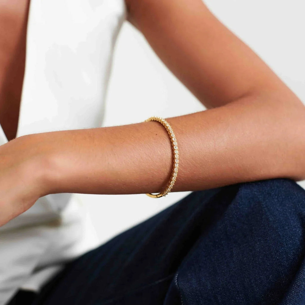 Close-up of a gold and diamond tennis bracelet worn on a woman's arm with a white top and dark jeans