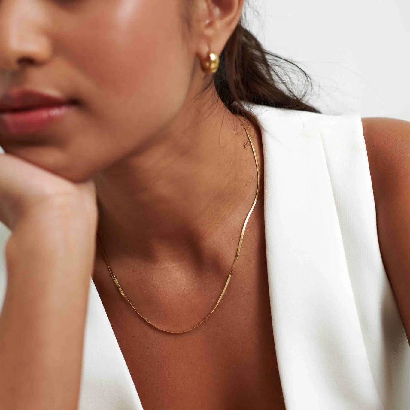 Close-up of woman wearing gold hoop earrings, thin gold necklace, and white sleeveless top