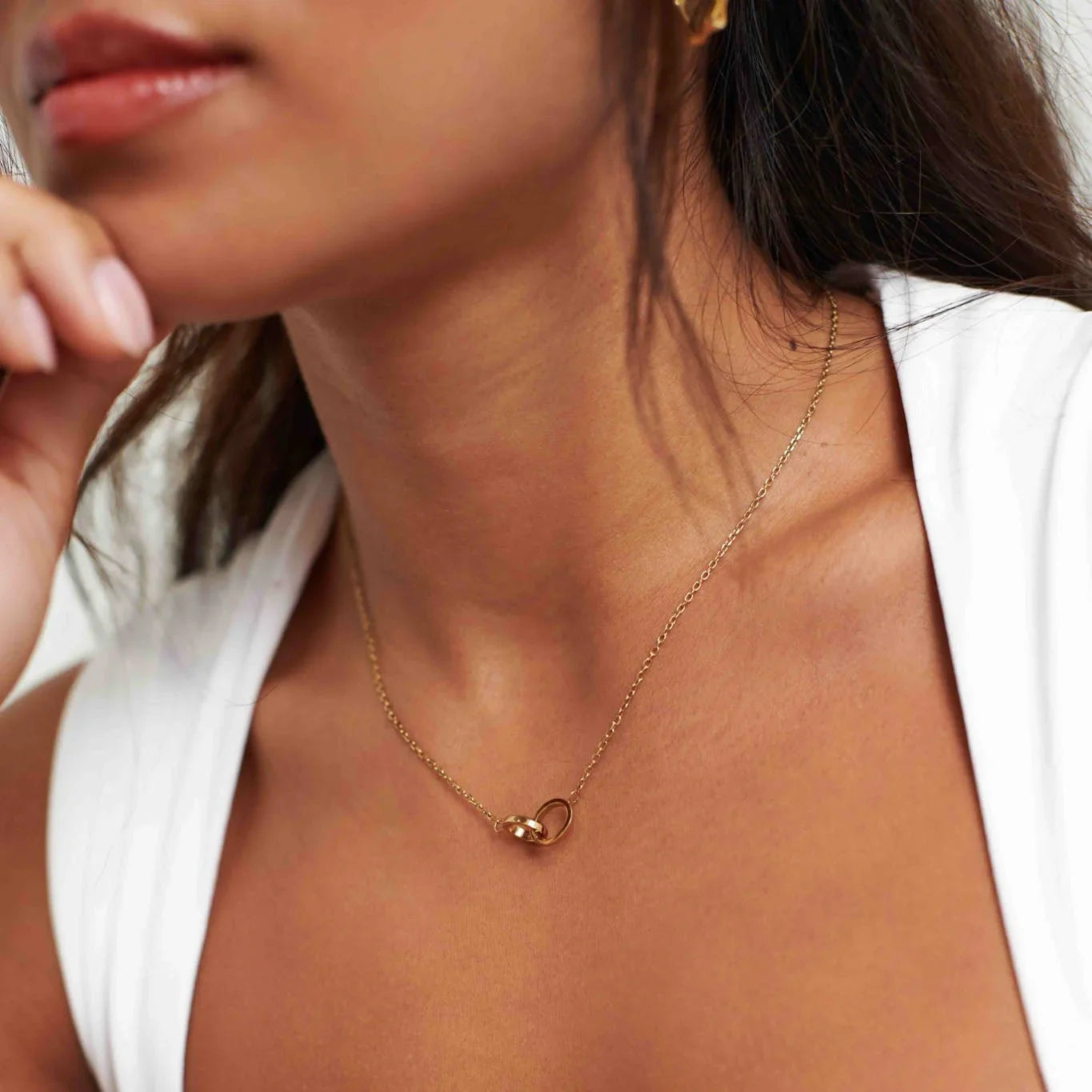 Close-up of woman wearing gold necklace with linked circle pendant and white sleeveless top
