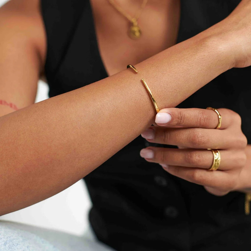 Close-up of person wearing gold open cuff bracelet, gold rings, and black sleeveless top
