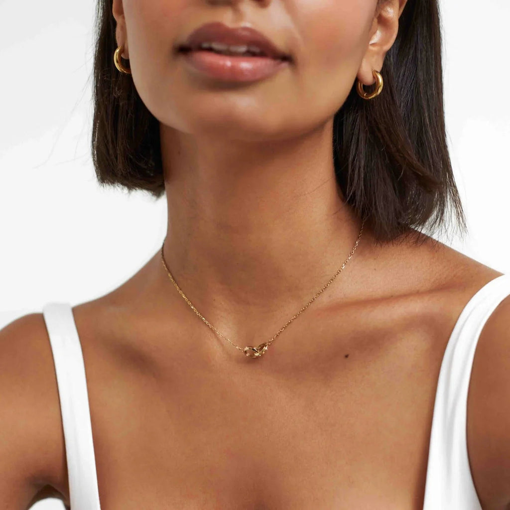 Close-up of woman wearing gold hoop earrings and a delicate gold chain necklace with interlocking links