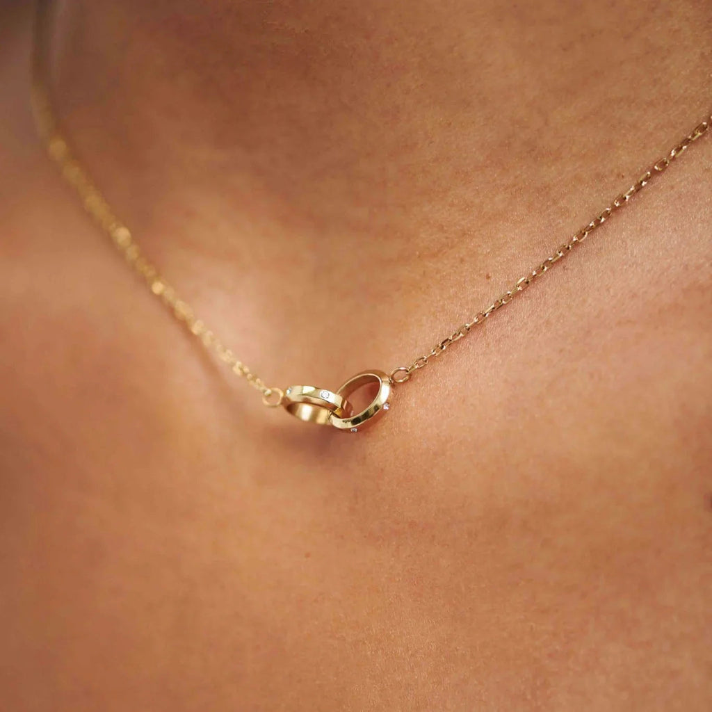 Close-up of gold necklace with two interlocking diamond-studded rings on skin