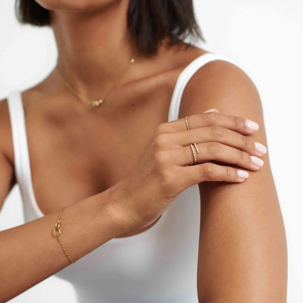 Woman in white tank top wearing minimalist gold jewelry including rings, bracelet, and necklace
