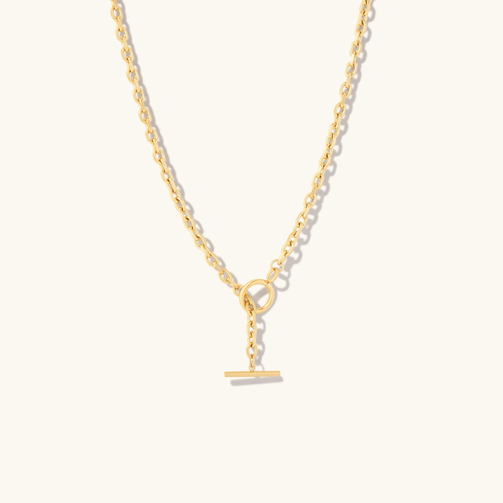 Gold chain necklace with toggle clasp on beige background