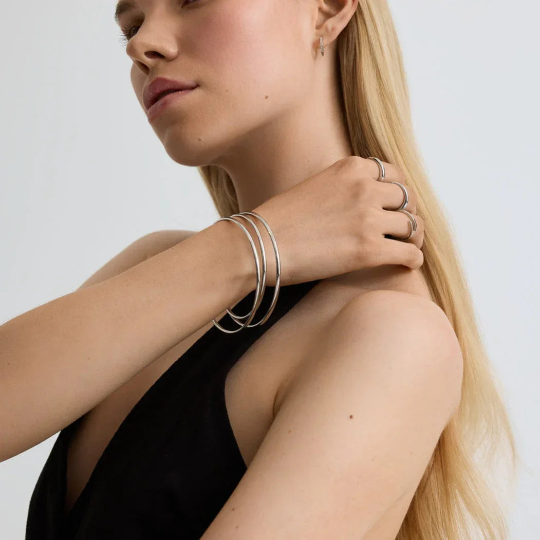 Blonde woman wearing minimalist silver bangles and rings with black sleeveless top on light background
