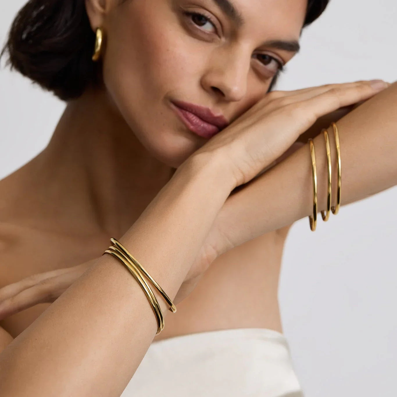 Woman wearing minimalist classic gold bangles and gold hoop earrings with a neutral background
