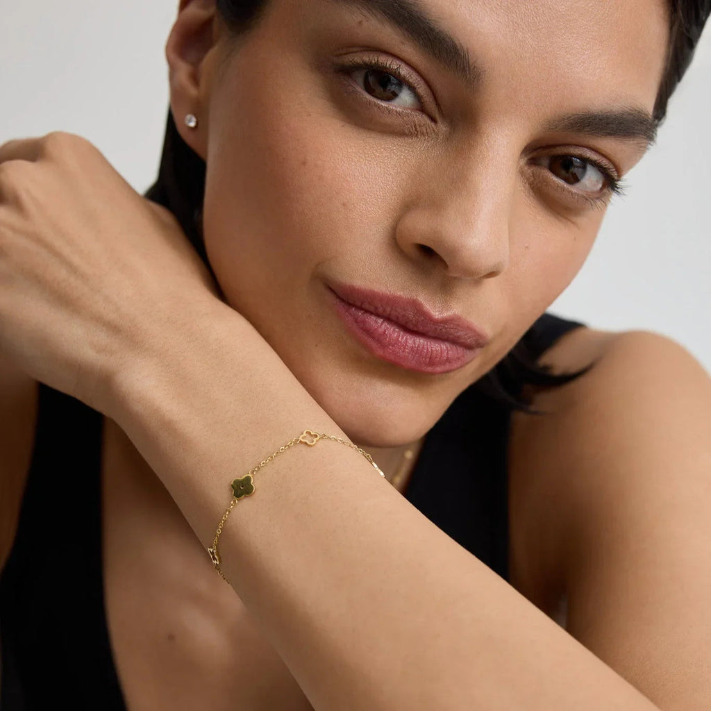 Close-up of woman wearing delicate gold clover charm bracelet and small stud earrings