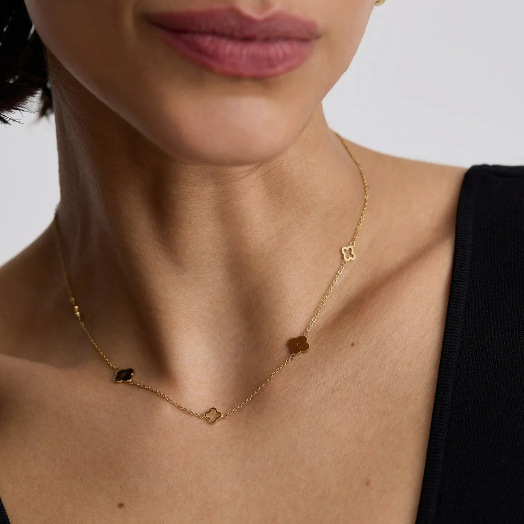 Close-up of a woman wearing a delicate gold clover necklace with small four-leaf clover charms