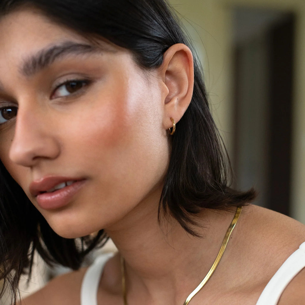Close-up of a woman with short dark hair wearing a small gold hoop earring and gold necklace