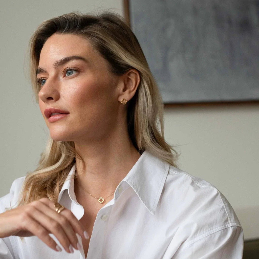 Portrait of a blonde woman in a white shirt wearing gold clover-shaped necklace and earrings