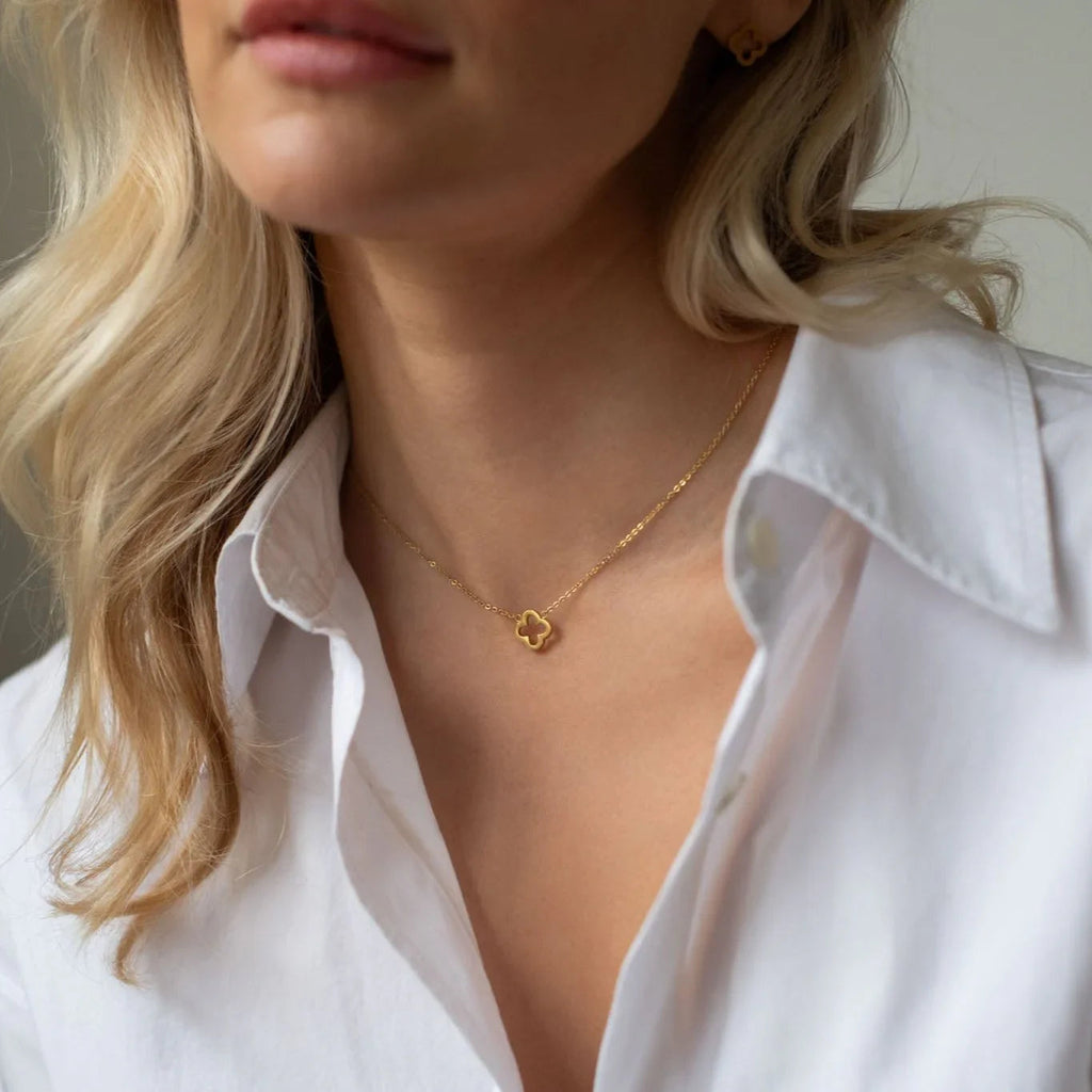 Close-up of woman wearing gold clover pendant necklace and white shirt with blonde hair detail
