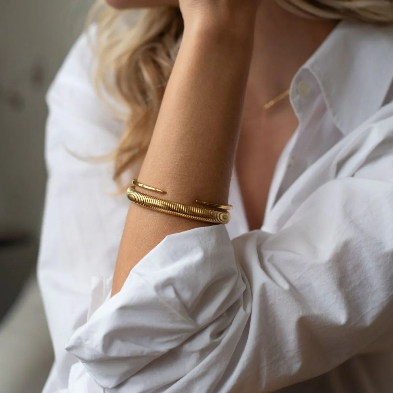Close-up of woman wearing elegant gold coil bangle and open cuff bracelet with white shirt