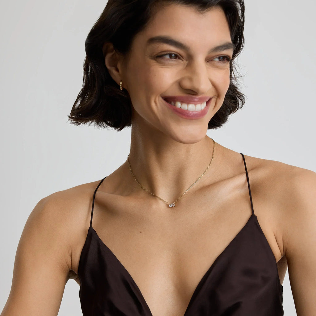 Smiling woman wearing a delicate gold necklace with two small pendants and matching gold earrings