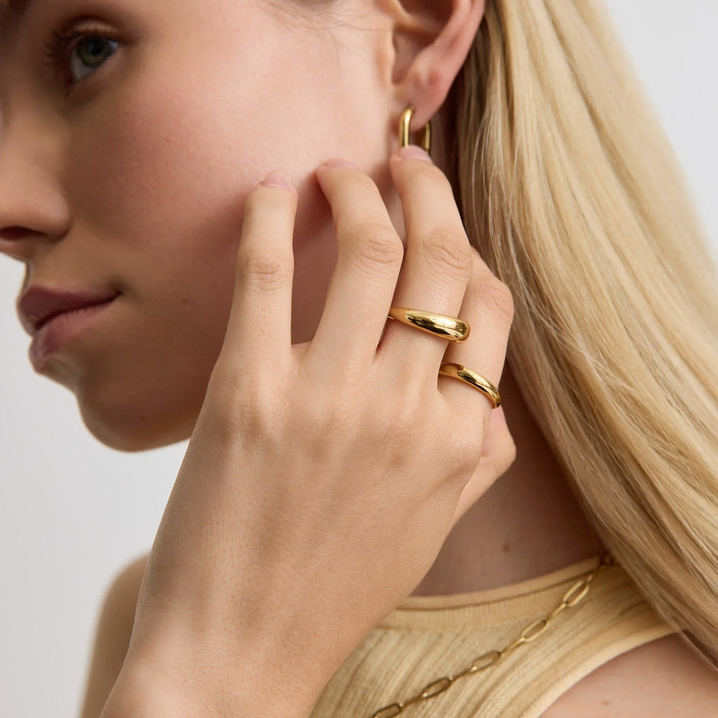 Close-up of woman's hand with two gold dome rings and matching gold hoop earrings