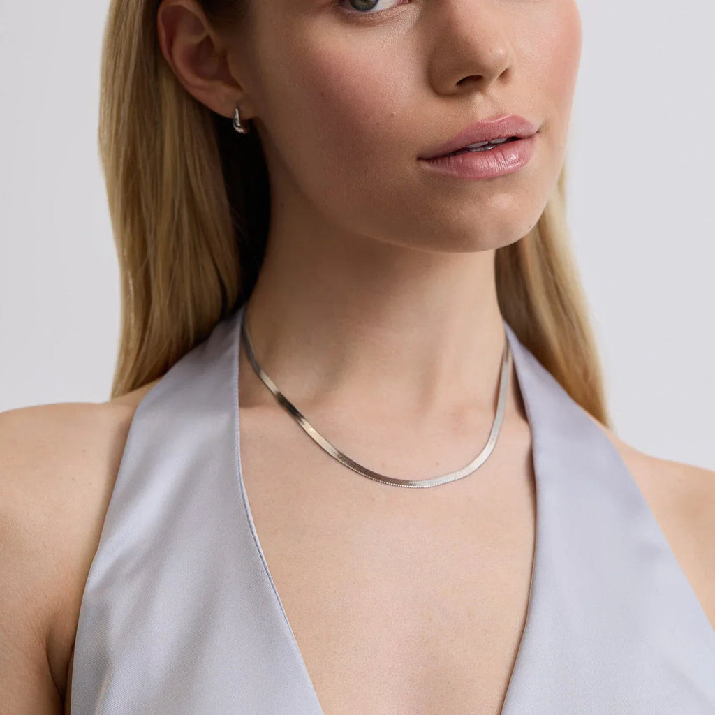 Close-up of woman in light gray halter top wearing sleek silver necklace and small silver hoop earring