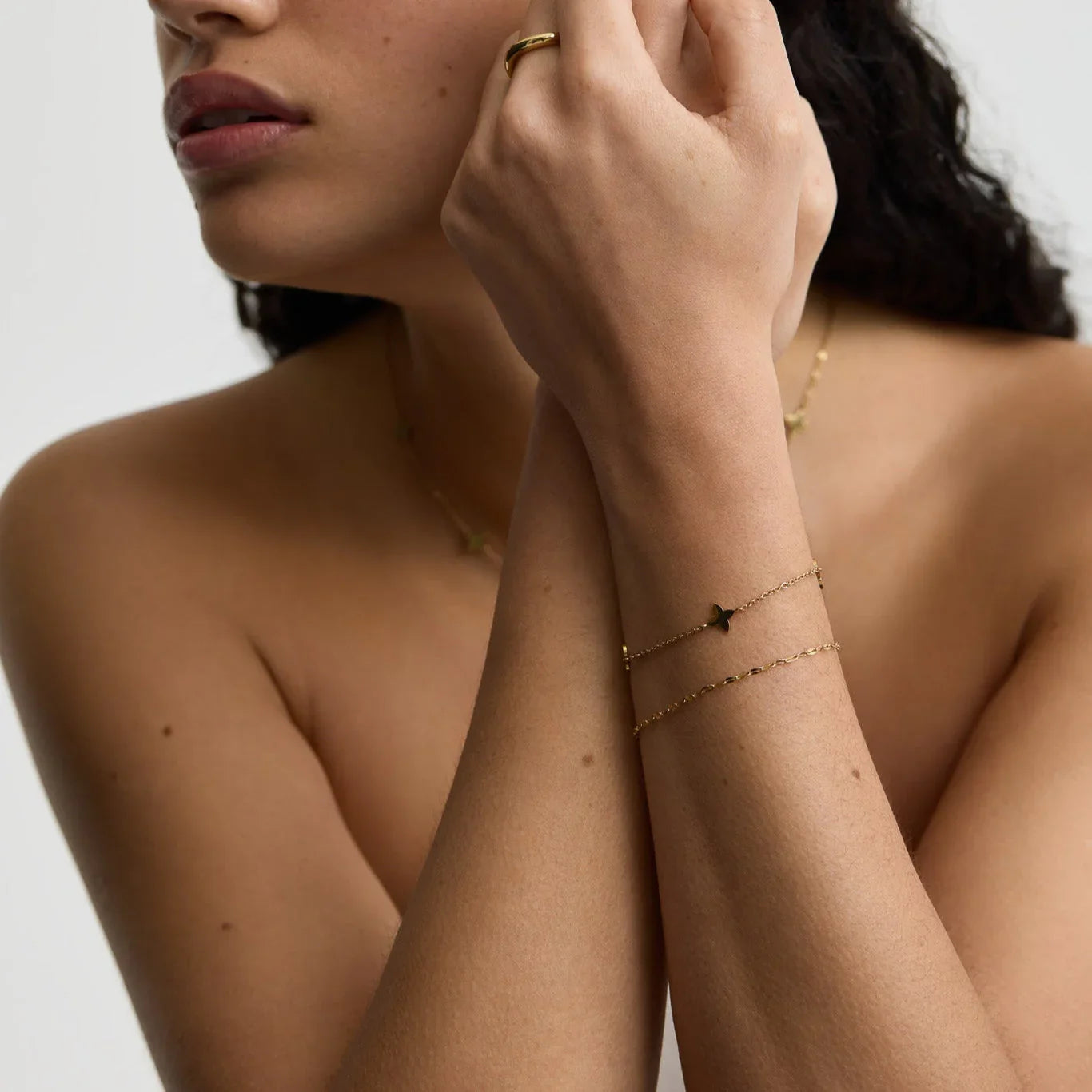 Close-up of woman wearing delicate gold butterfly bracelet, gold ring, and necklace on bare skin