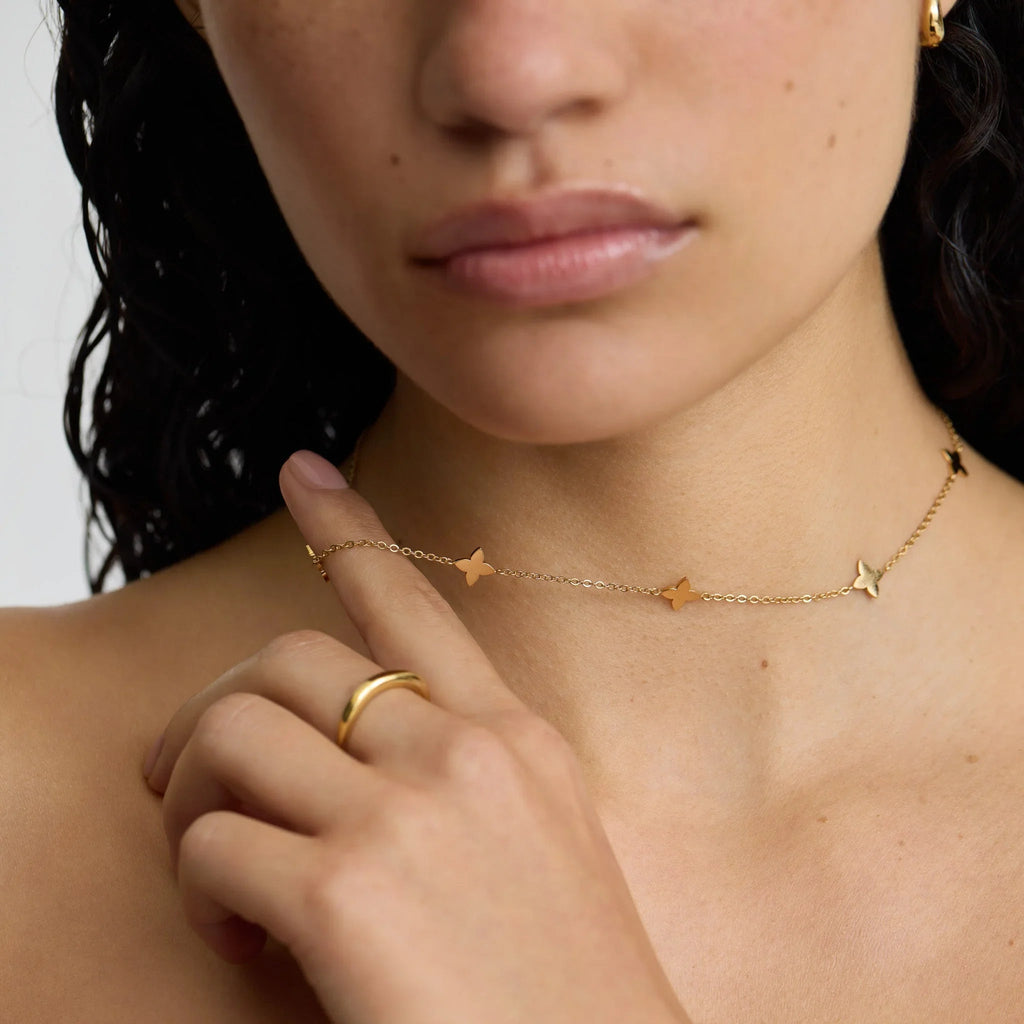 Close-up of woman wearing delicate gold butterfly necklace and gold ring