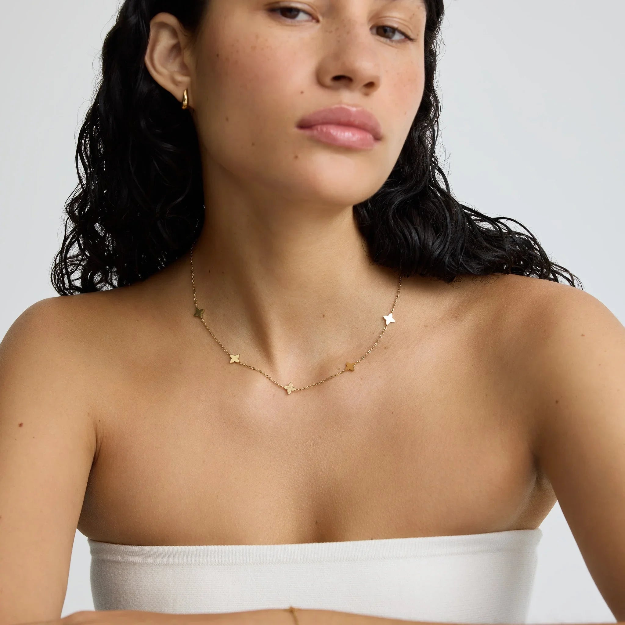 Close-up of woman wearing gold butterfly charm necklace and gold hoop earring with natural makeup