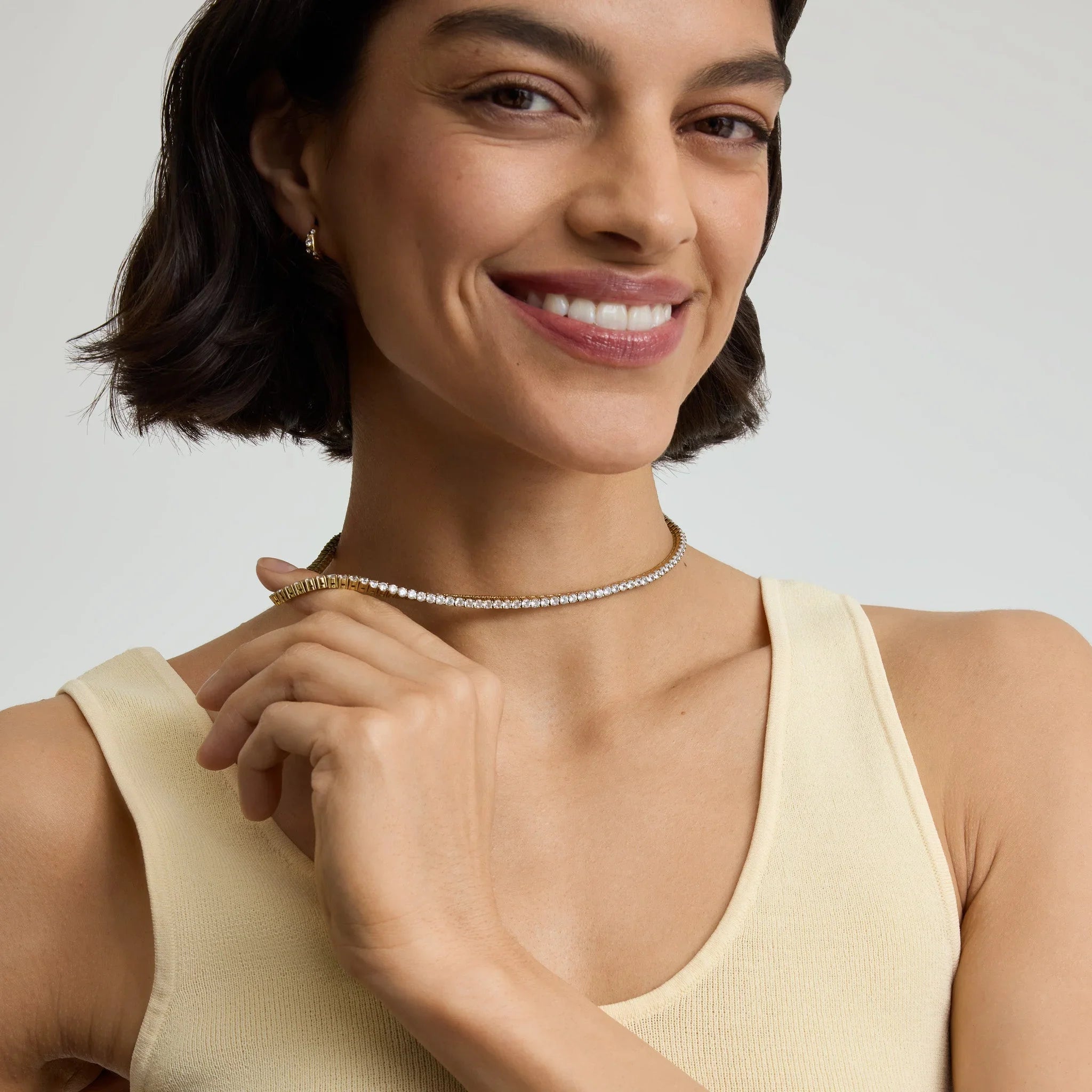 Smiling woman wearing a two-tone lux tennis necklace with gold and silver diamonds, beige tank top