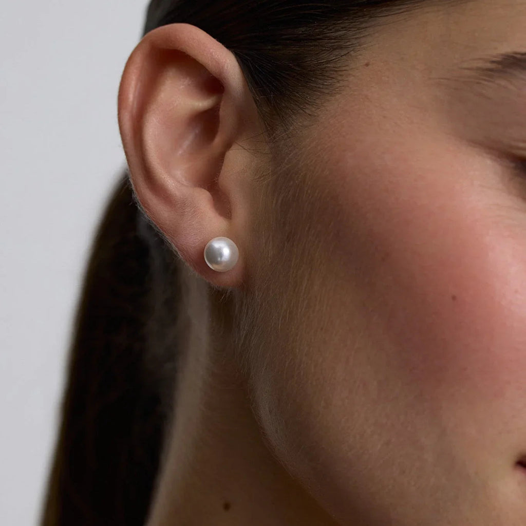 Close-up of a woman's ear wearing a single large white pearl stud earring