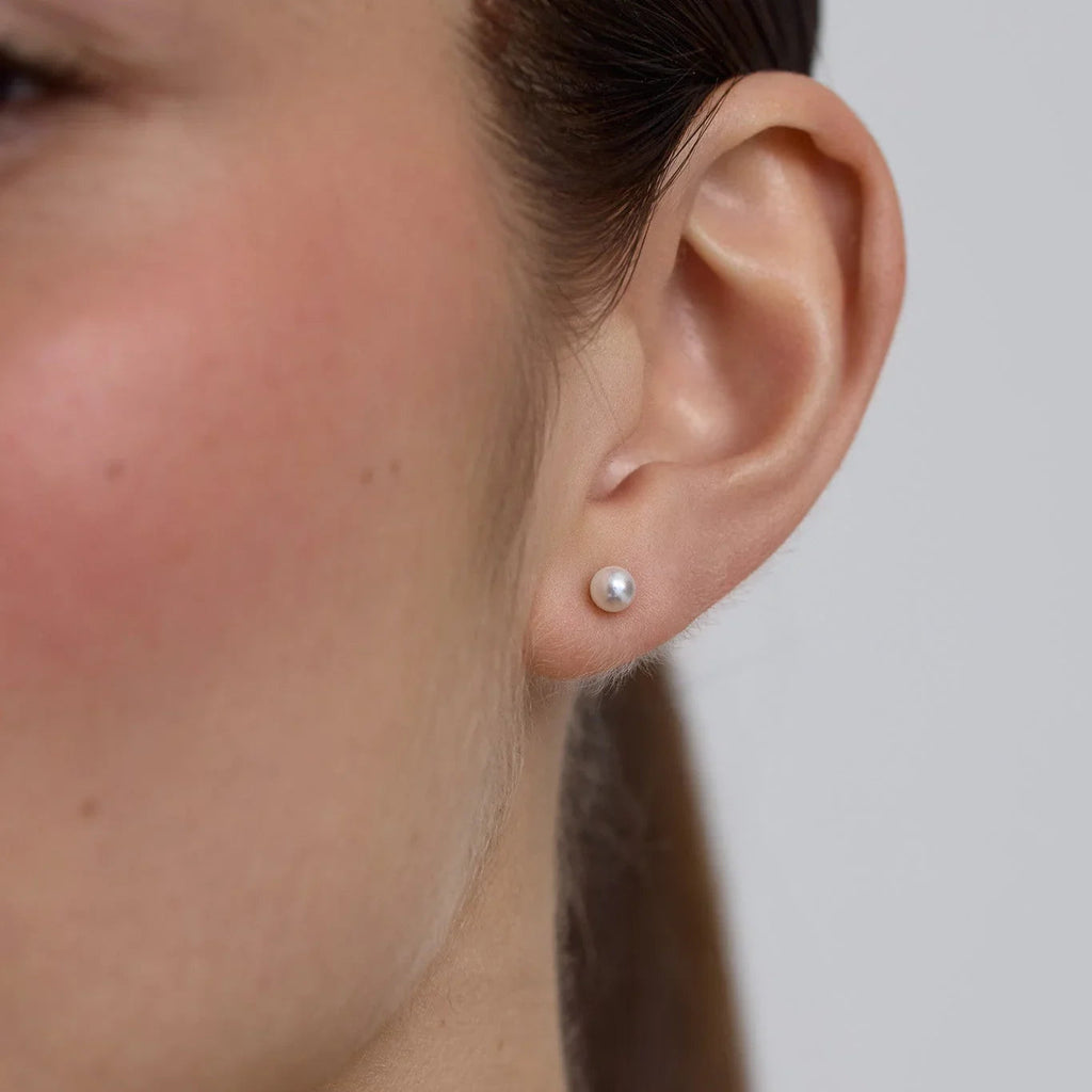 Close-up of a woman's ear wearing a small white pearl stud earring against a gray background