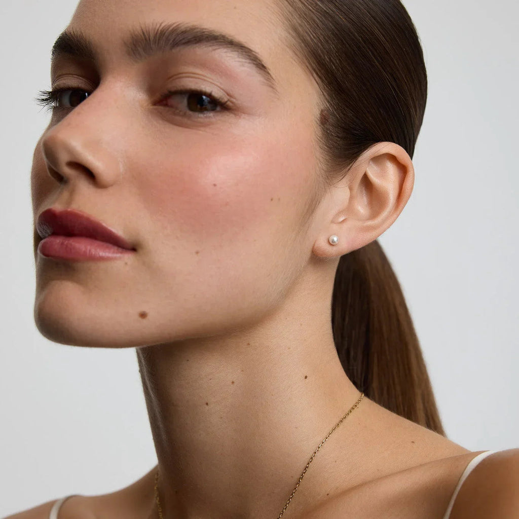 Close-up of woman wearing small pearl stud earrings with natural makeup and sleek ponytail