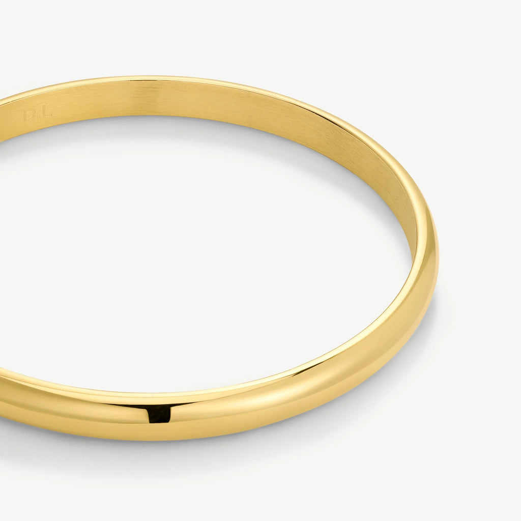 Close-up of a polished gold bangle bracelet with a smooth, shiny surface on white background