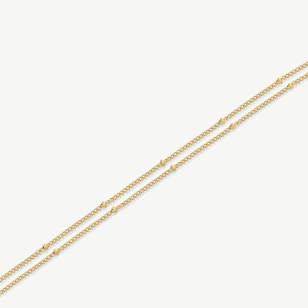 Delicate double-layered gold chain necklace with small gold bead accents on white background