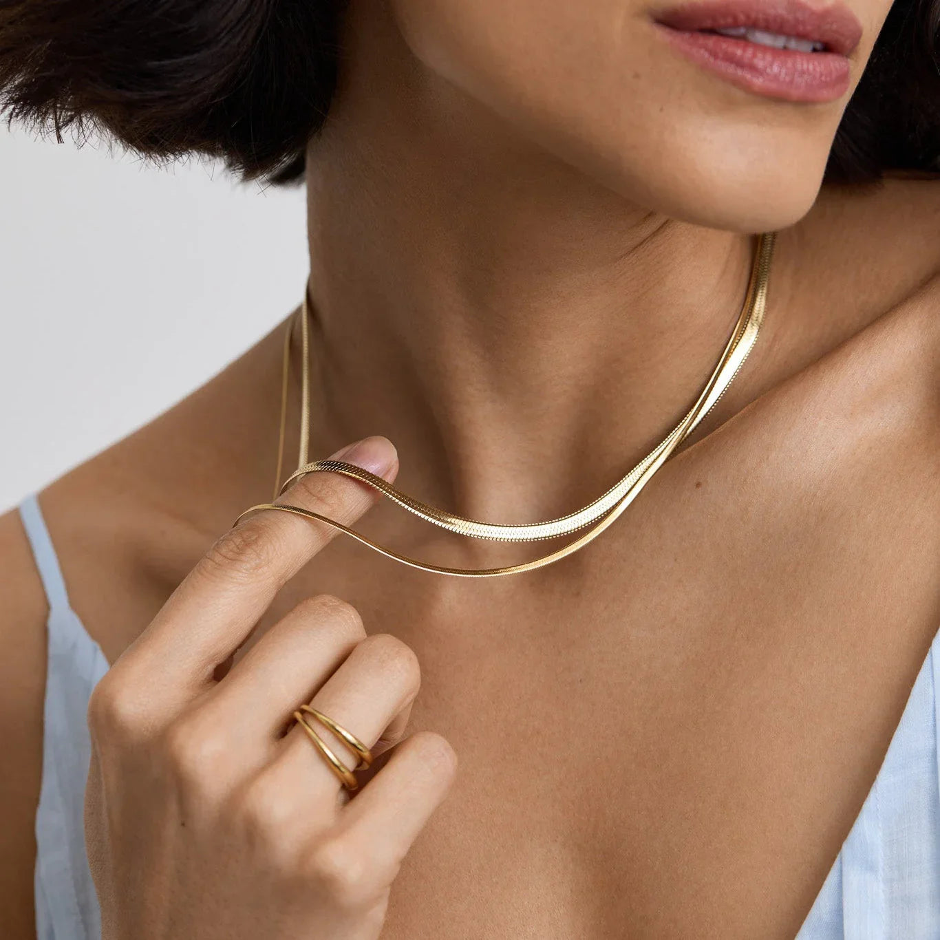 Close-up of woman wearing a shiny gold snake necklace and a gold ring, dressed in a light blue top