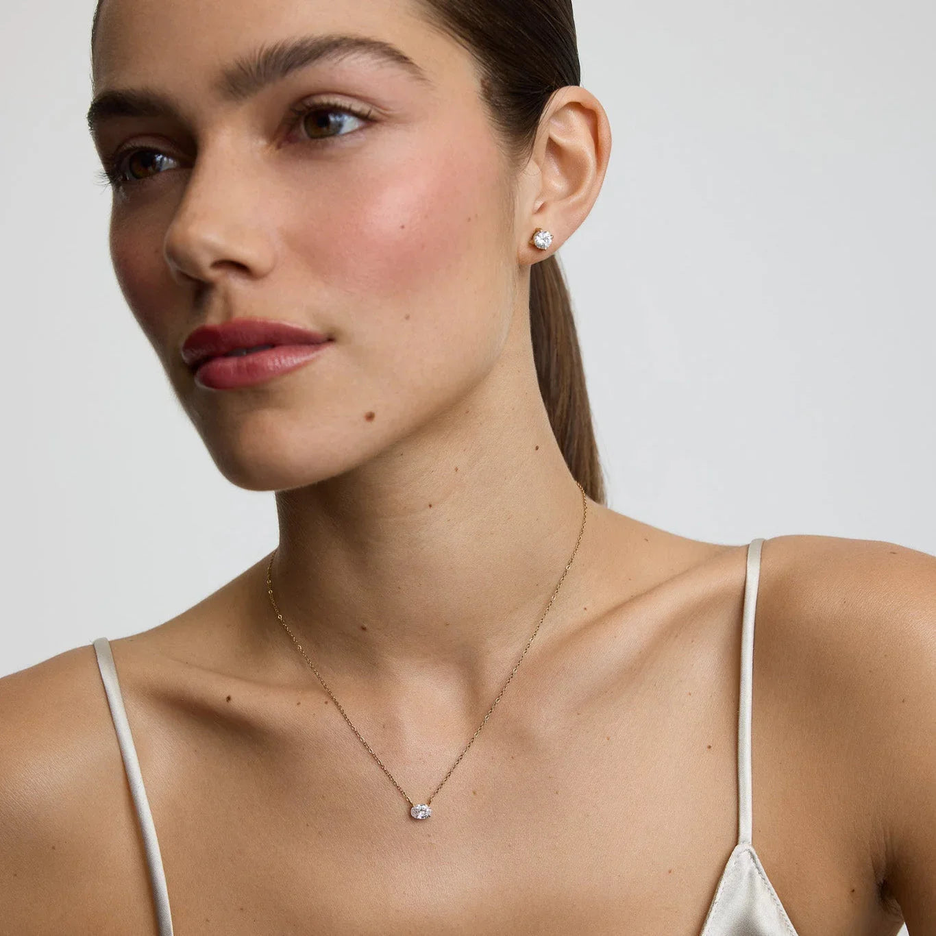 Woman wearing diamond stud earrings and matching solitaire diamond necklace with thin gold chain