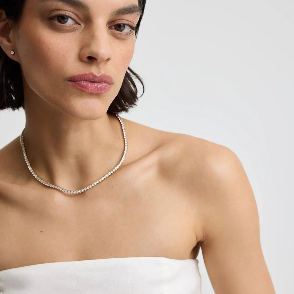 Close-up of woman wearing a diamond tennis necklace and stud earrings on bare shoulders